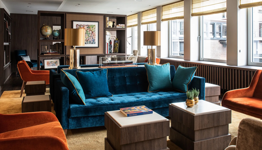 Interior Studio Isabella Hamann Contract Interior; HOTEL SPEICHERSTADT HAMBURG, lobby/reception in blue and orange tones. It has a blue velveted sofa, with blue pillows on top, and a deep orange armchairs next to it.