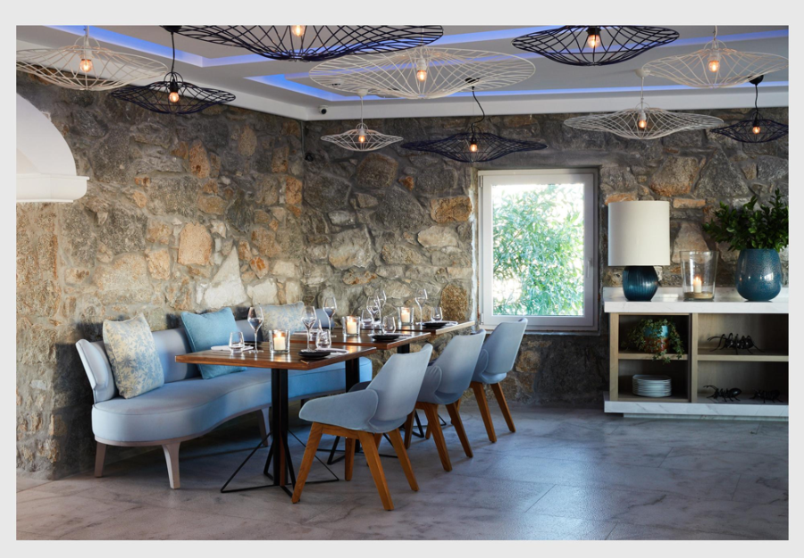 Designhotels, Myconian Kyma, Mykonos, Greece by Studio Linda Ehrl bar with a blue sofa, 3 blue dining sofas and several chandeliers on the wall.