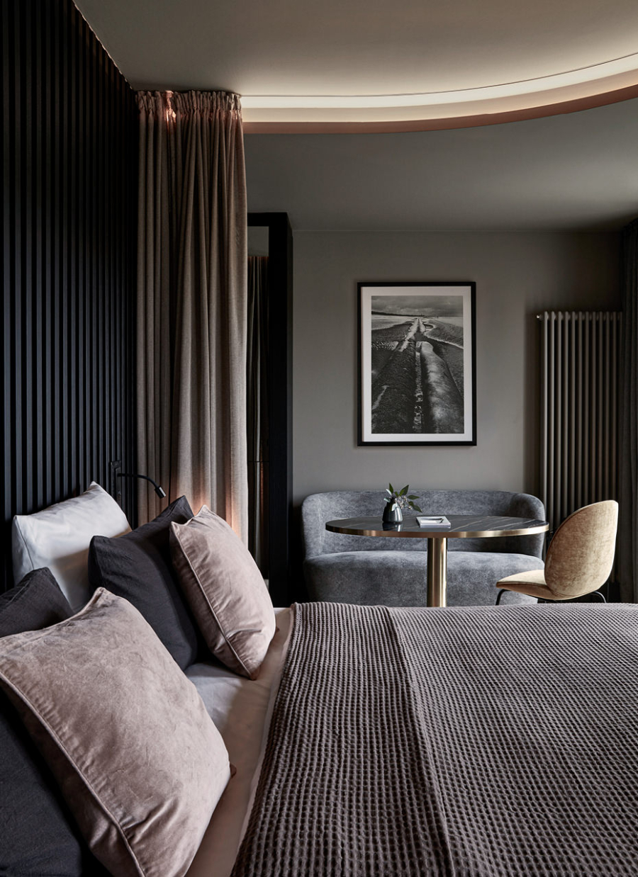 Lambs and Lions, Mauritzhof Hotel suite bedroom with a grey sofa, and a gold armchair
